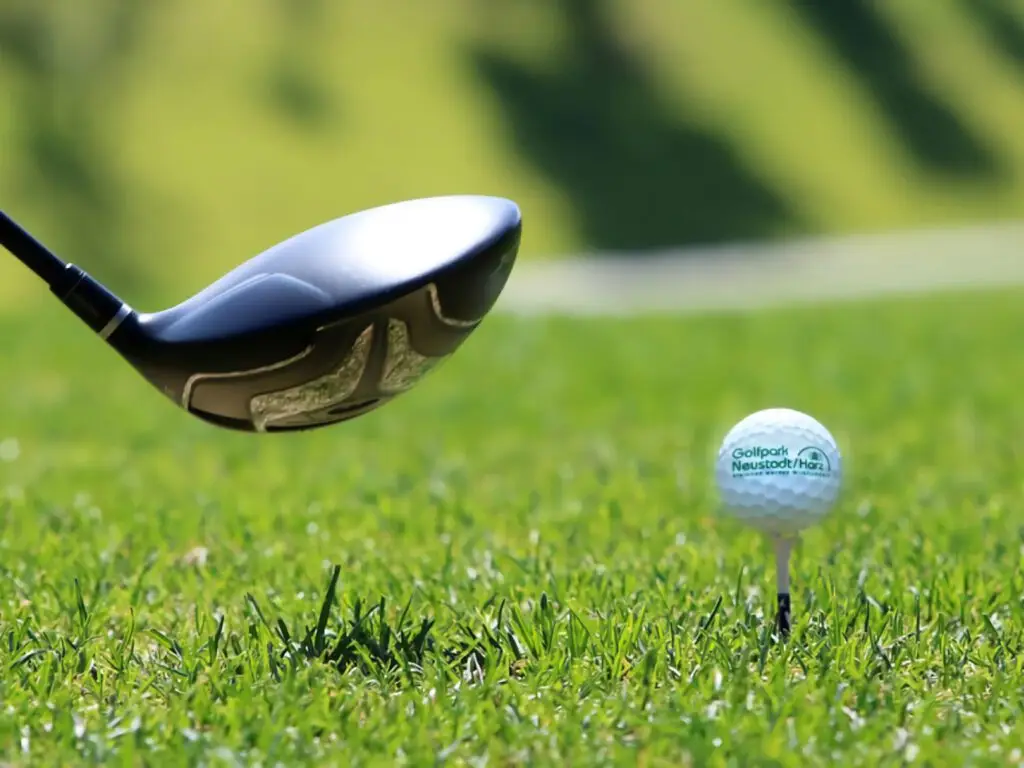 Nahaufnahme eines Golfschlägers, der einen Golfball mit dem Logo des Golfpark Neustadt/Harz vom Tee abschlägt.