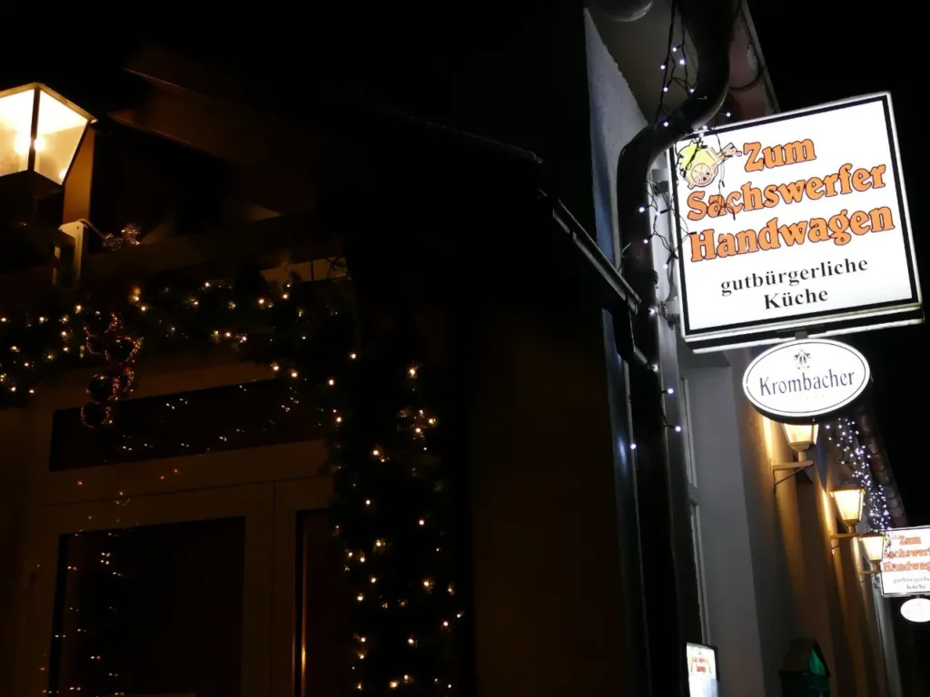 Außenansicht der Gaststätte "Zum Sachswerfer Handwagen" bei Nacht, mit beleuchtetem Werbeschild