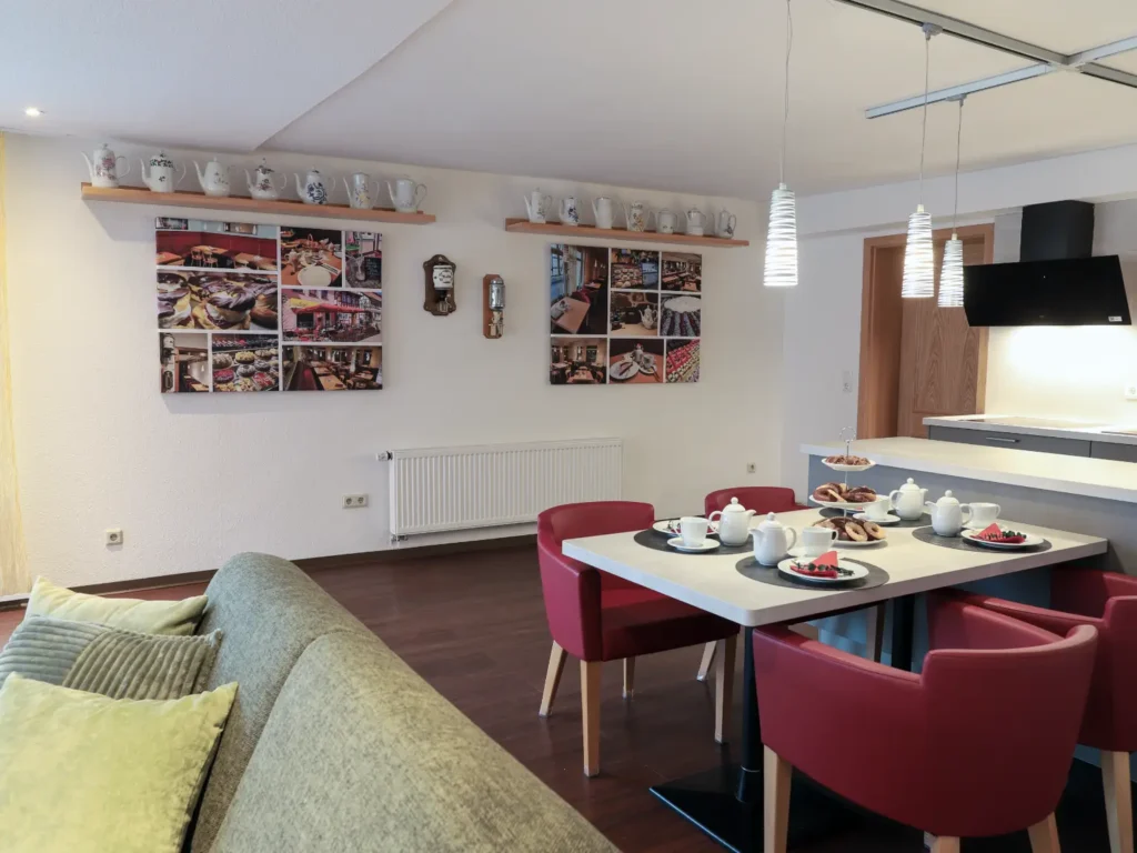 Moderne Küche mit Kochinsel und Theke, darüber historische Wandbilder aus der ehemaligen Konditorei König und eine Teekannen-Sammlung.