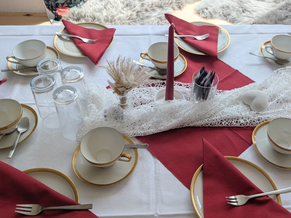 Festlich gedeckte Kaffeetafel im Fräulein Fuchs und Hummel mit weißer Tischdecke, roten Servietten, goldrandigem Porzellan und Kerze – buchbar für private Feiern.