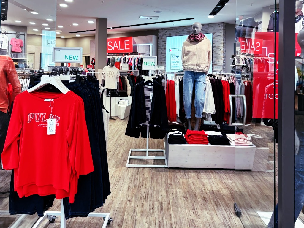 Blick in Mode Koch in der Nordhäuser Marktpassage: Rotes Cecil-Shirt mit Aufschrift „PULSE“, Schaufensterpuppe mit Teddyjacke und Schal, Sale-Schilder und Street-One-Display.